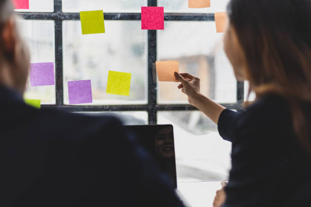 istock Businessmen and colleagues brainstorming scheduling business strategy, planning work in the office with paper stickers on the glass. 1800445013