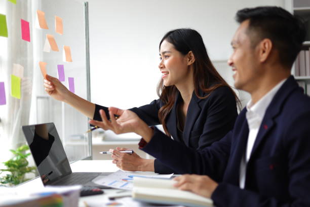 istock Businessmen and colleagues brainstorming scheduling business strategy, planning work in the office with paper stickers on the glass. 1800445018