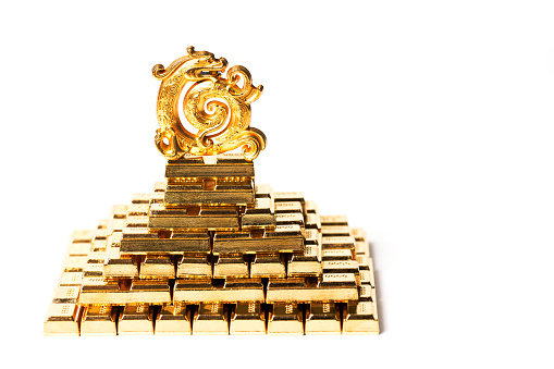 Golden traditional Chinese dragon figurine on a pyramid of gold bars on a white background