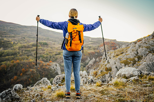 Cheerful hiker woman with hiking poles standing on a mountain top, admiring the view