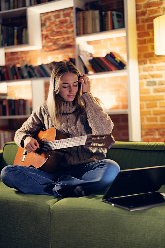 Teenage girl playing guitar at home. The girl is sitting on a sofa.
Shot with Canon R5