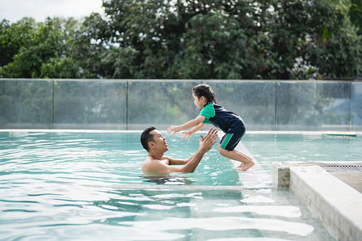 Father and daughter kid girl child swimming playing in the pool, smiling and laughing. Having fun in the pool at water park, family happy concept. Water activity for children on summer holiday.