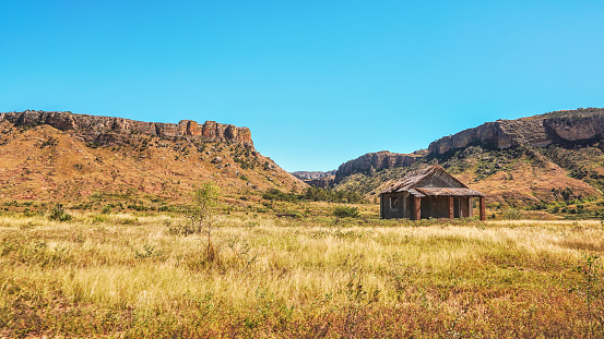 Low grass growing on African savanna, small rocky mountains in background, simple house near  - typical scenery at Isalo national Park, Madagascar