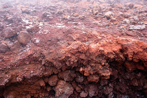 Close-up of red lava rock on Mount Etna crater, Sicily island in Italy. Warm volcanic lava stone formation and smoke from crater of active volcano.