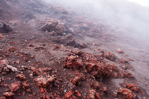 Close-up of red lava rock on Mount Etna crater, Sicily island in Italy. Warm volcanic lava stone formation and smoke from crater of active volcano.