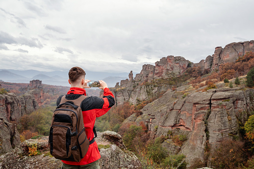 Young hiker taking pictures with his phone at the mountain peak