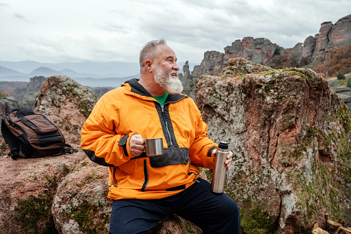 Mature bearded tourist resting and drinking coffee in the mountains