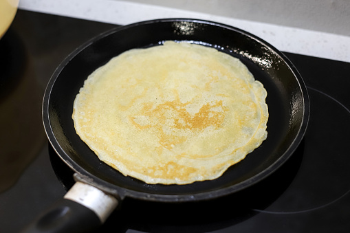 Making bliny at home. High angle view of traditional tasty thin pancake on the frying pan. Photo with selective focus
