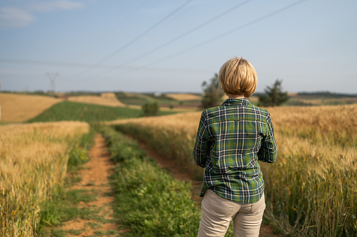 Mature woman farmer standing by the agricultural fields outdoors.