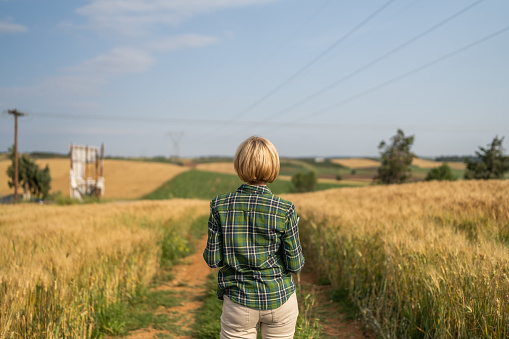Mature woman farmer standing by the agricultural fields outdoors.