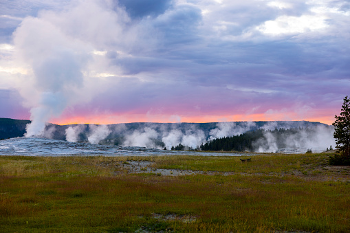 Old Faithful is a famous geyser in Yellowstone National Park that erupts regularly and spectacularly. At night, it is a sight to behold, as the jet of boiling water and steam is illuminated. This photo is late at night near civil twilight with a spectacular red sunset.