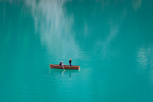 Lago di Braies, Italy - October 18, 2023: Tranquil scene of two people in a rowboat on a turquoise-coloured lake in the Alps. Minimalist image.
