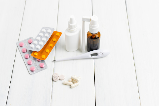 Cold remedies, medicines, thermometer, capsules and pills in a blister pack on wooden table. Healthcare concept, home treatment of flu and coronavirus.