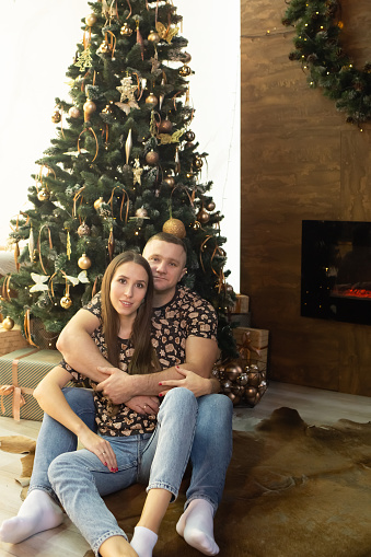 a beautiful couple is sitting in the living room near a beautiful Christmas tree. young family waiting for Christmas and New Year.