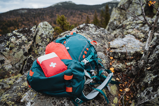 A red hiking first aid kit is on a backpack in the mountains, tourist equipment. High quality photo