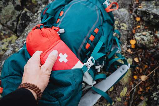 A tourist takes out a red first aid kit, a first aid kit, and camping equipment from a backpack pocket. High quality photo