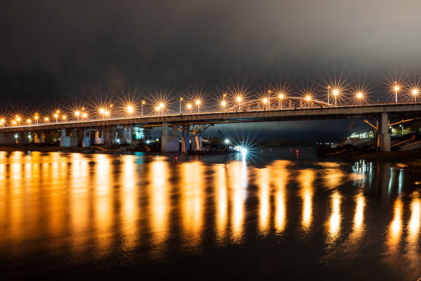 Bridge over the river illuminated by lanterns, reflection of lantern light on the water surface, road place night photo. Beautiful glare of lanterns.
