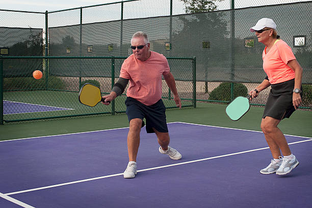 Mixed Doubles Pickleball Action - Smooth Backhand Colorful image of mixed doubles team playing in a pickleball match. pickleball stock pictures, royalty-free photos & images