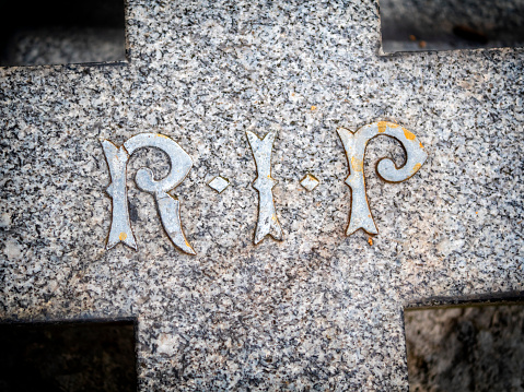 Part of a granite cross in a suburban cemetery, bearing the initials R.I.P - “Requiescat in Pace” - Rest in Peace.