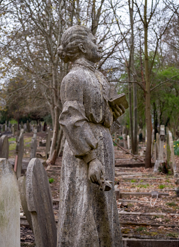 A generic figure of a woman holding a prayer book or bible in her left hand, plus a rose in her right hand, on a grave in a suburban cemetery. Such figures were very popular during the late 19th and early 20th centuries and were made of reconstituted and moulded stone. This example has survived without much damage apart from natural weathering.