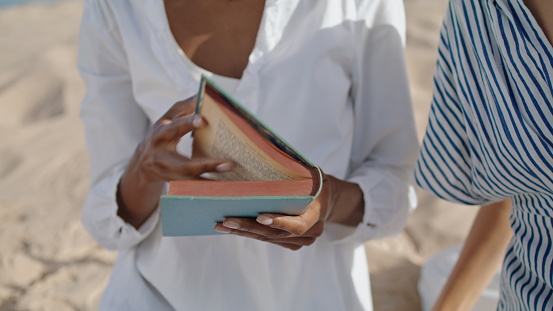 Closeup hands open book pointing page beach picnic. Relaxed girls read romance