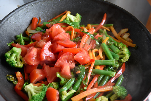 Stir fried vegetables in a pan at home. Mixing various vegetables in a pan closeup. Broccoli, green beans, peppers, tomatoes, carrots, kale