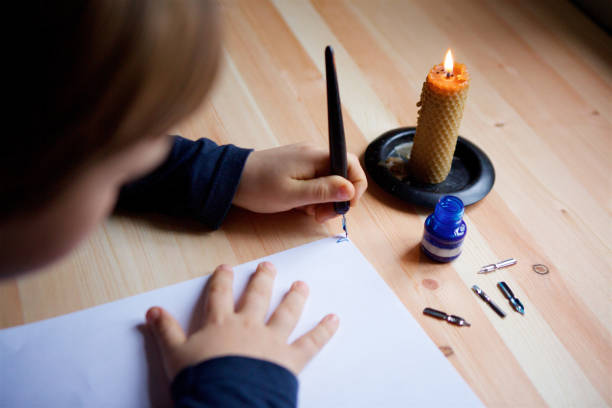 istock Children's hands write letters on white paper with an ink pen. 1800733092