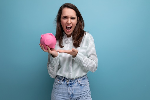smiling attractive european brunette young lady keeps money in a pink piggy bank.