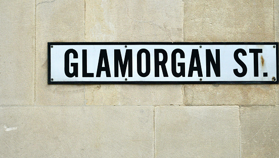 Glamorgan Street sign depicting the name of a street which can be found in Brecon town centre in the Brecon Beacons in Wales. Black writing on a white sign fixed to a stone wall