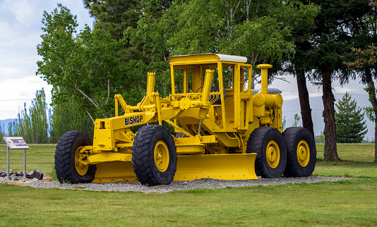 Twizel, New Zealand - 4 November, 2023: A vintage yellow grader with BISHOP printed on its side, displayed outdoors with trees in the background. Part of the Twizel Heritage Trail collection.
