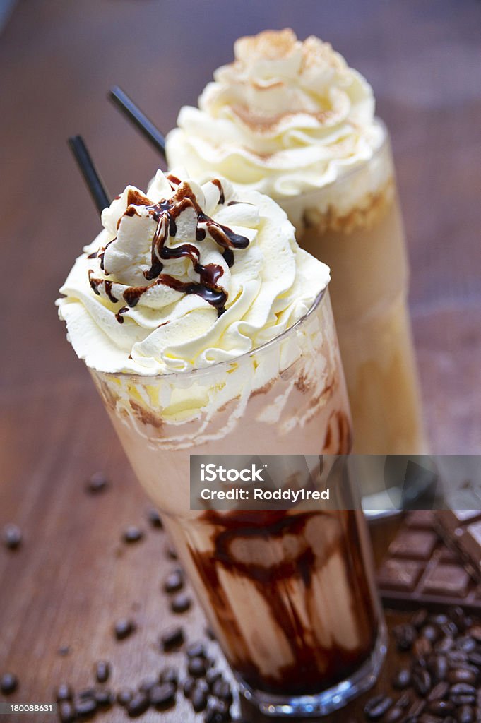 Chocolate and Caramel Milkshakes Delicious chocolate and caramel milkshakes topped with cream and sauce, on a wooden counter. They stand among cocoa beans and slabs of chocolate. Chocolate Milkshake Stock Photo