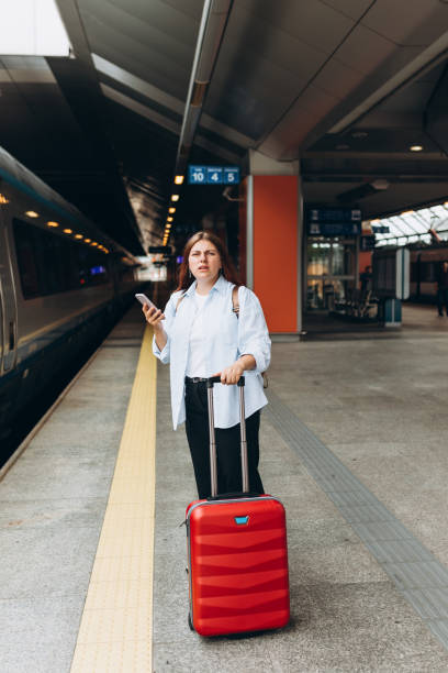 istock Young refugee redhhead woman crying and waiting train on station platform, she lost and using smart phone. Railroad transport concept 1800905489