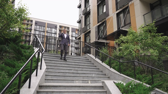 Smiling businessman talking on the smartphone while going down the stairs outdoors. Business, communication, technology concept. Slow motion