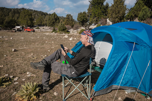 Adult man looking at his phone in front of his tent.