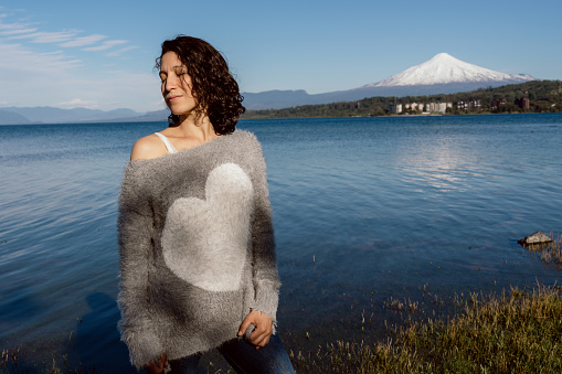 Latin woman enjoying sunny afternoon on shore of lake with snowy mountains in background