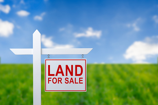 Beautiful green field and blue sky with LAND FOR SALE sign.