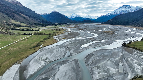 Aerial drone scenery of the braided Dart river flowing through a rural valley bordered by the Southern Alps mountains into Lake Wakatipu near Glenorchy