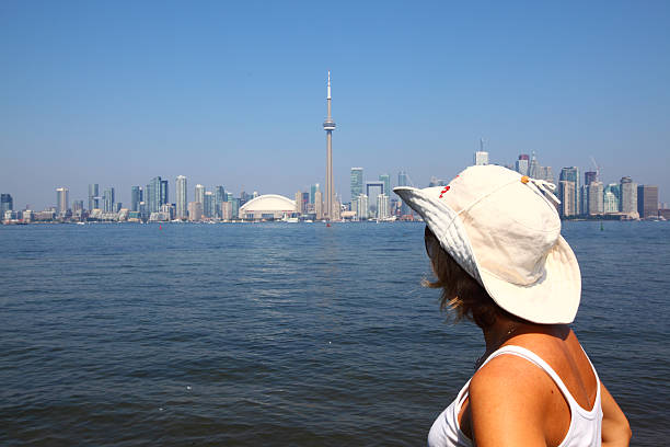 Young female looking at Toronto skyline from the Toronto islands in August on a beautiful sunny day with blue sky, lake Ontario and wonderful Toronto CN Tower and other major buildings on the background. Tourists in Toronto. Toronto as a travel destination. Toronto tourism. Landmarks of Toronto.