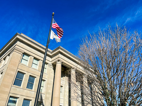 Looking up at the exterior of the Appellate Court of the State of Illinois District Building in Springfield, Illinois, USA. The American flag and the State of Illinois flag fly high against the sky. Vivid clear blue skies overhead.
