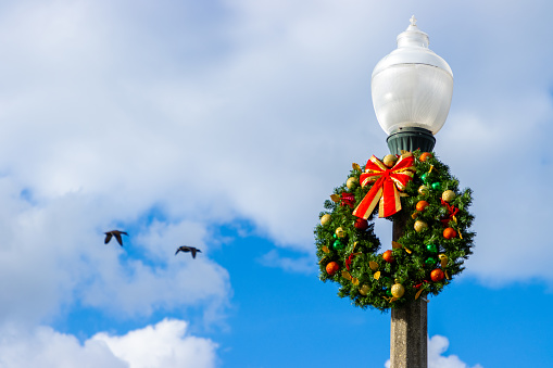 A festive Christmas holiday wreath hanging on an outdoor street lamp post.