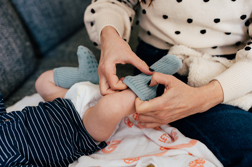 A close up view of an unrecognizable Caucasian female putting socks on to her adorable little child.