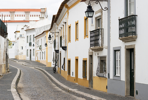 Street in Evora, Portugal. Ancient cobblestone road with stone pavements either side and historic houses on the right side. The narrow road winds it way through this historic Portuguese city.