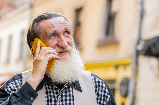 Senior mature man tourist having remote conversation communicate speaking by smartphone with friend. Elderly old grandfather talking on phone unexpected good news gossip walking in urban city street