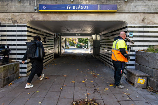 Stockholm, Sweden Oct 19, 2023 A city employee cleaning the entrance to the Blasut tunnelbana or Metro station.and a passenger walking by.