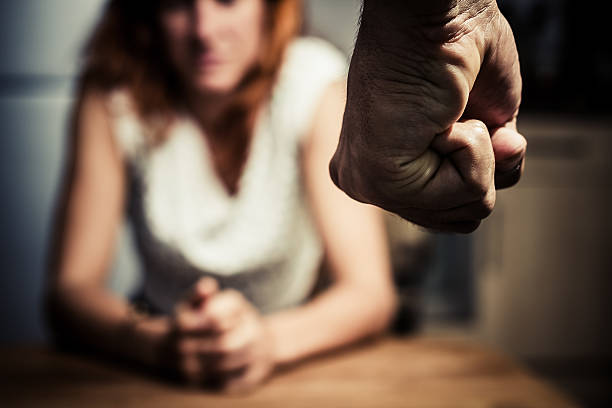 Woman in fear of domestic abuse Young woman is sitting hunched at a table at home, the focus is on a man's fist in the foregound of the image abuse stock pictures, royalty-free photos & images