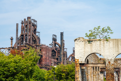 Sunlight beams through the rusty structure of the Steelstacks, an abandoned steel factory in Bethlehem, Pennsylvania. The intricate ironwork and the grand scale of the industrial age, now silent and still, set against a clear sky at sunset