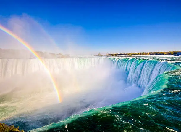 A rainbow shows in the bright daytime mist that hangs around Niagara Falls, viewed from Ontario, Canada.