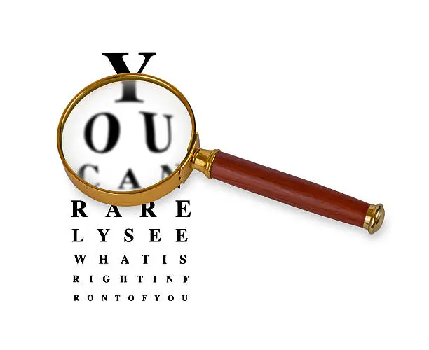 Magnifying glass in front of a funny eyetest chart. Eyetest in background is sharp while vision through magnifying glass lens is blurred. Magnifying glass has golden rim and wooden handle.