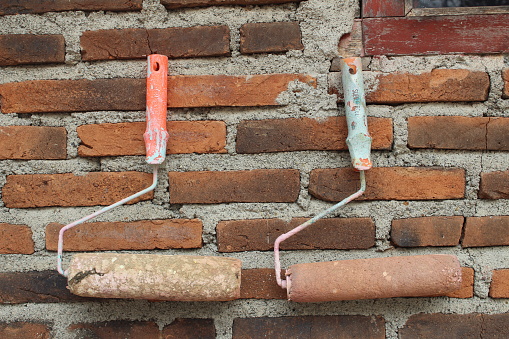 two used paint rollers hanging on a red brick wall