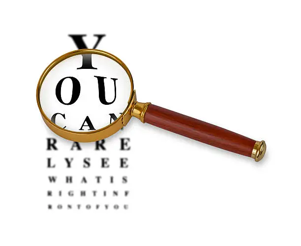 Magnifying glass in front of a funny eyetest chart. Eyetest in background is blurred while vision through magnifying glass lens is sharp. Magnifying glass has golden rim and wooden handle.